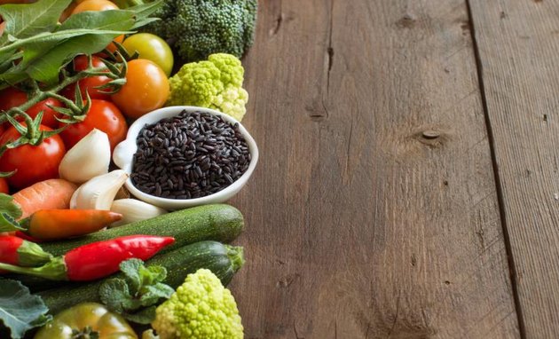 Uncooked black rice in a bowl with vegetables on wood