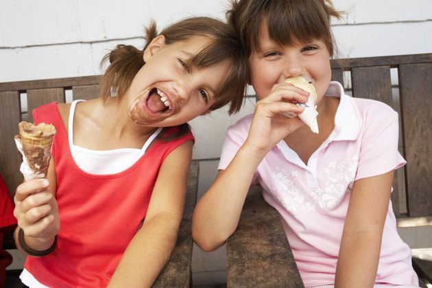 Two girls (6-9) eating ice cream, laughing, close-up, portrait