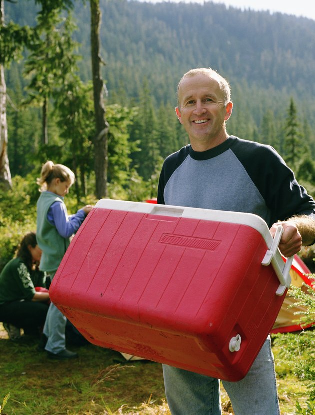 Father at camping site with family, carrying cooler, portrait