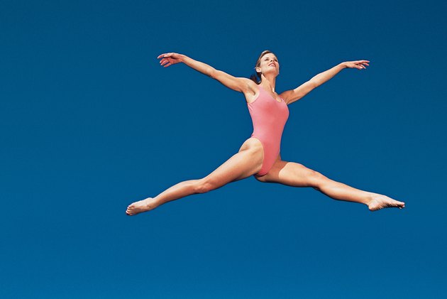Woman in leotard leaping across sky