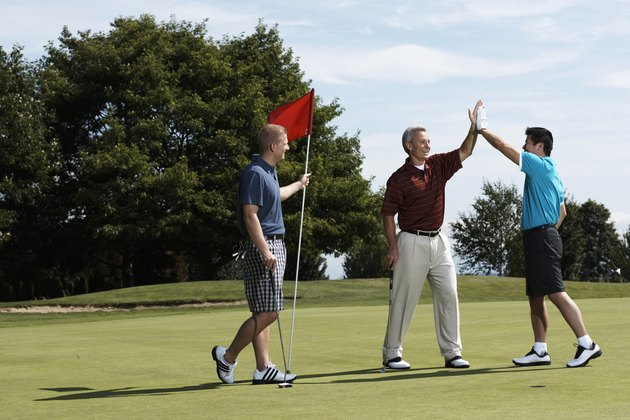 Golfers high fiving on putting green standing next to golfer holding flag