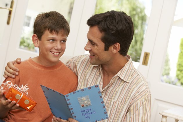 Father holding card by son (10-12) holding present, smiling