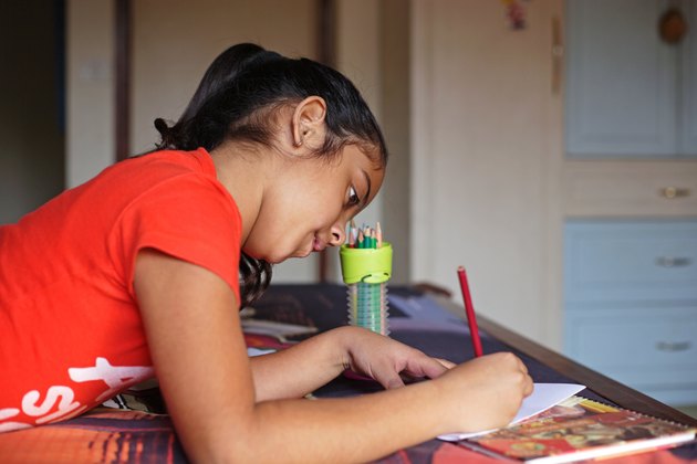 Girl sitting on bed, drawing on a paper