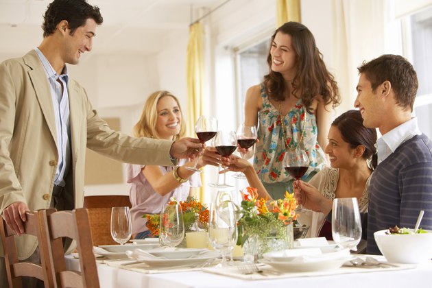 Group of young people raising glasses at dinner table, smiling