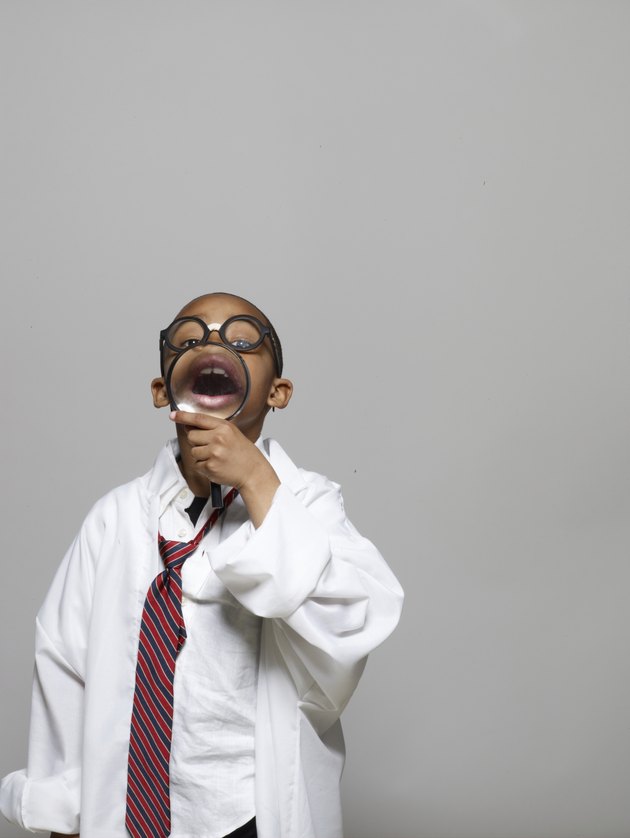 Boy (5-7) in lab coat, holding magnifying glass, opening mouth wide