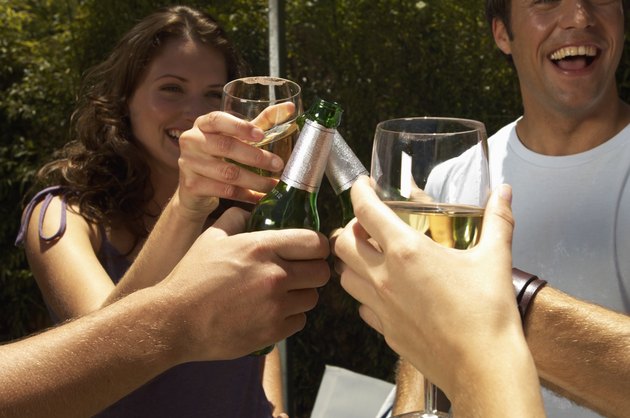 Young women and men toasting drinks around bbq, close up