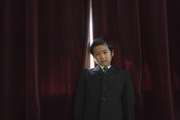 in suit in front of red curtains