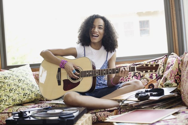 Teenage girl playing acoustic guitar and singing indoors