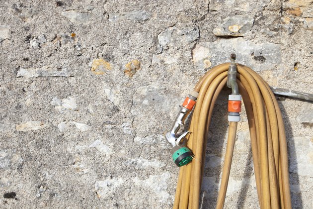 Coiled garden hose hanging on faucet against stone wall