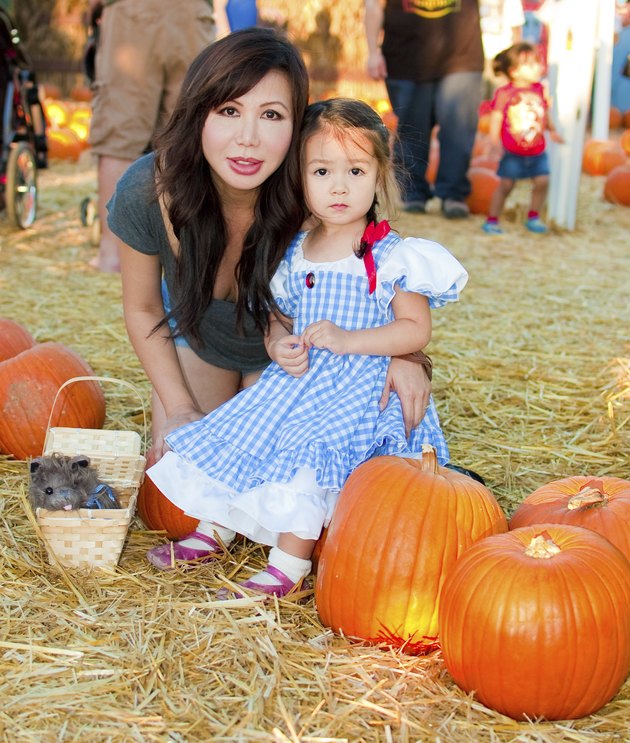 Asian mother and daughter visit a pumpkin patch, with the little one dressed up as Dorothy (from The Wizard Of Oz) for Halloween. And lets not forget her faithful little puppy in the basket.