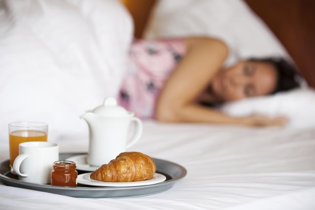 Frau schläft im Hotelbett und Frühstück steht bereit