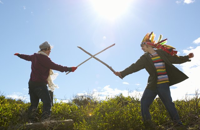 Teenage girl (16-17) and young man wearing feather headdress, duelling with sticks, side view