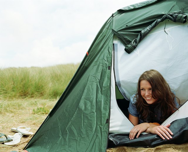 Young woman lying in tent opening, looking away, smiling