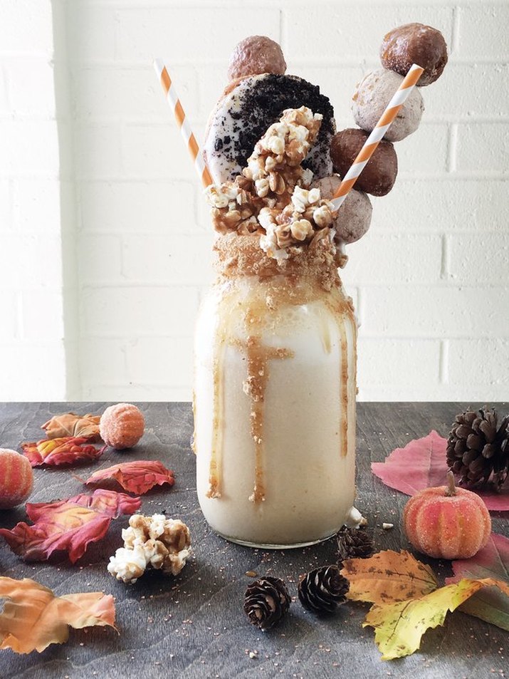 A pumpkin milkshake served in a mason jar, drizzled with caramel sauce and topped with extravagant garnishes