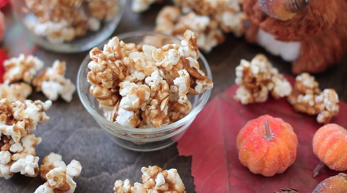 Pumpkin spice caramel corn in and around a small glass bowl, with miniature pumpkins alongside
