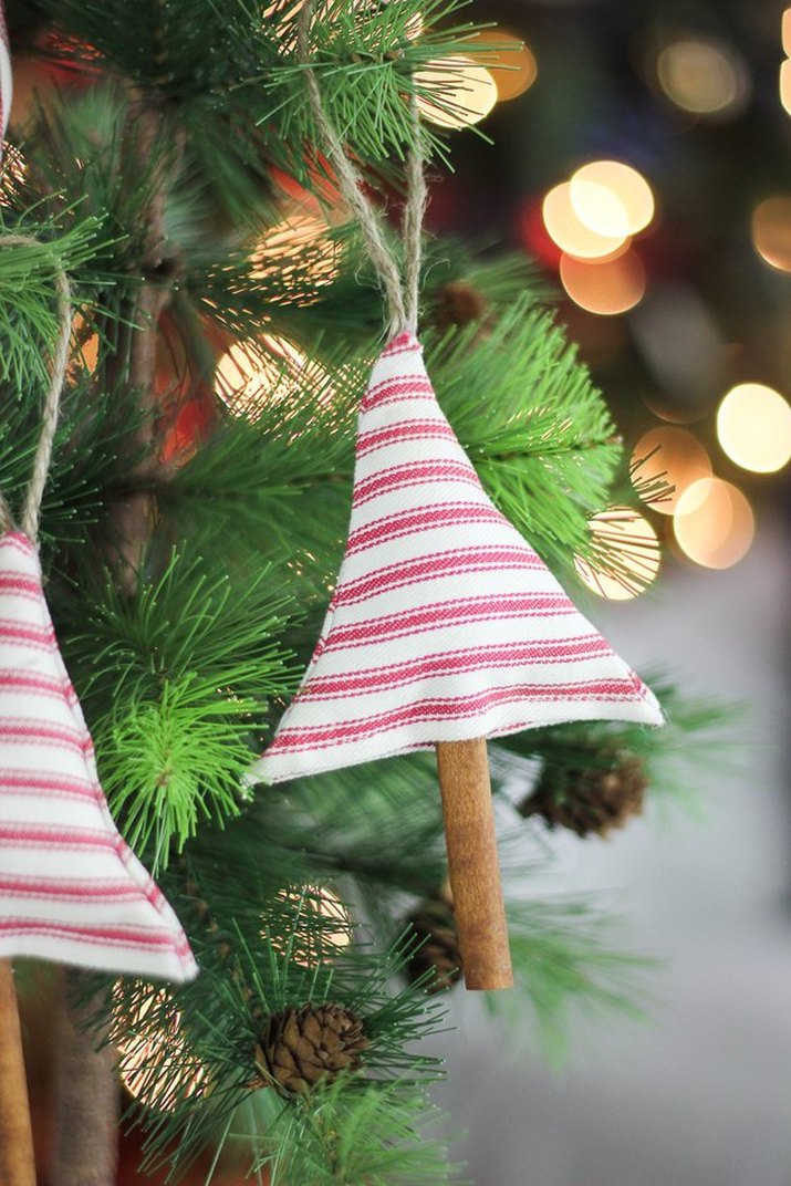Handmade ornaments of red and white striped fabric and a cinnamon stick, hanging on a Christmas tree
