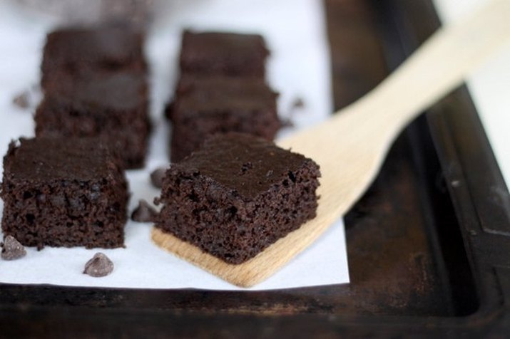 A brownie on a wooden spatula, with other baked, cut brownies displayed neatly on a parchment-lined sheet pan