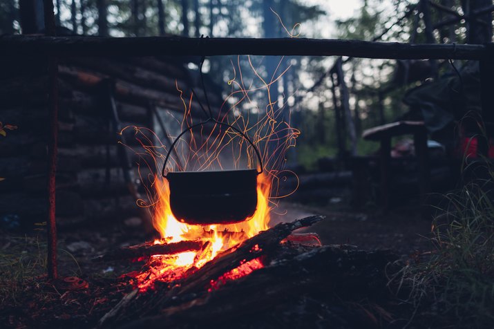 Container hanging over campfire in forest