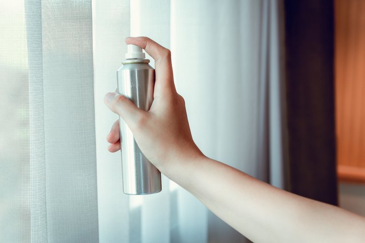 Cropped Hand Of Woman Spraying Air Freshener By Window
