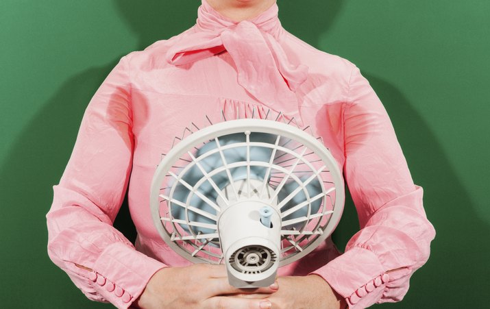 Midsection of businesswoman with sweaty armpits holding fan against green background