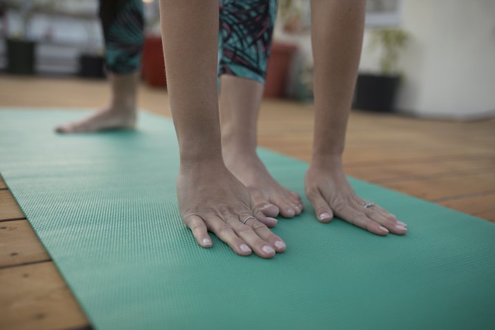 Close up woman practicing yoga on yoga mat with foot between hands
