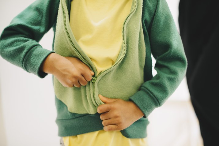 Midsection of boy zipping his jacket at home