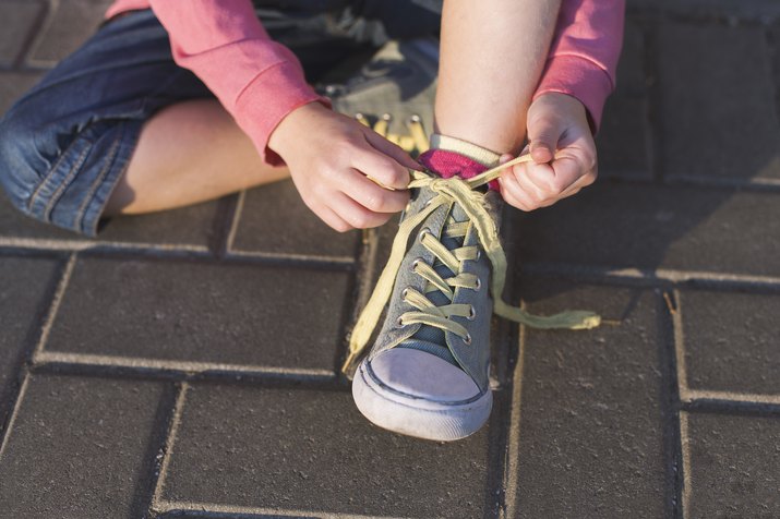 Girl sitting on ground tying her shoelaces