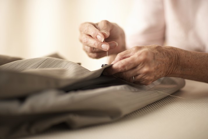 Senior woman sewing button on jacket, close-up of hands