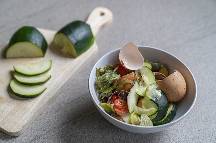 Bowl with food leftovers for the compost, with sliced zucchini on a cutting board in the background.