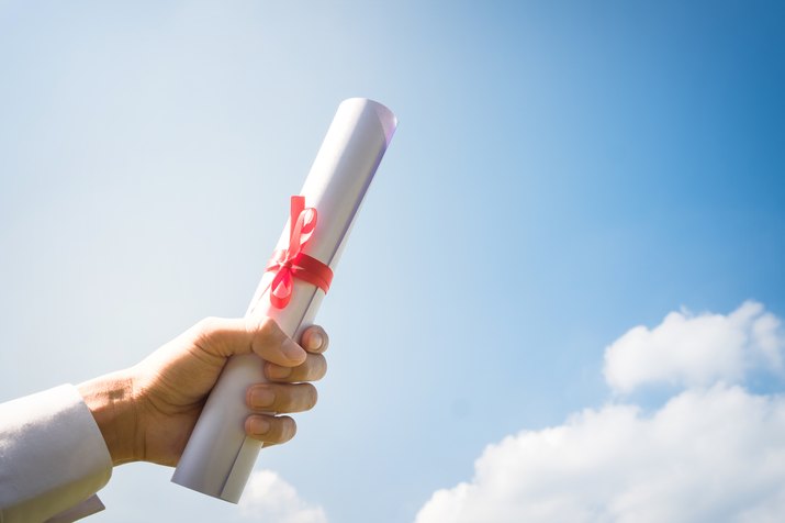 Hand holding Graduation certificate roll under the sunshine, blue sky background.