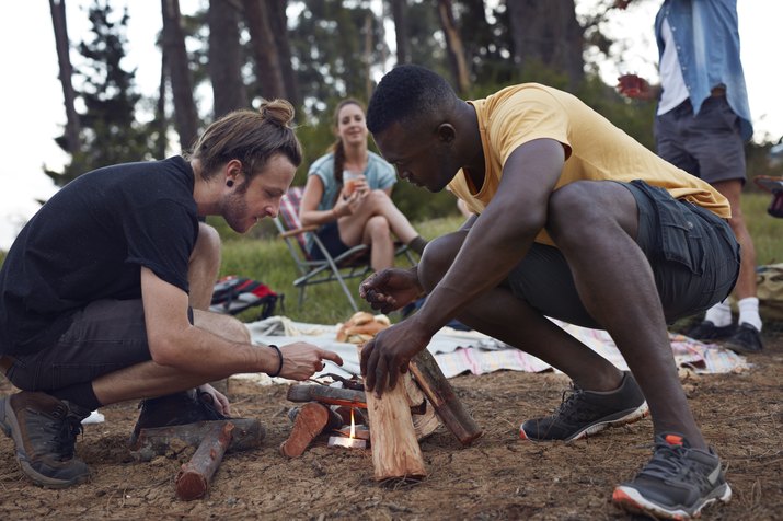 Friends lighting bonfire at campsite