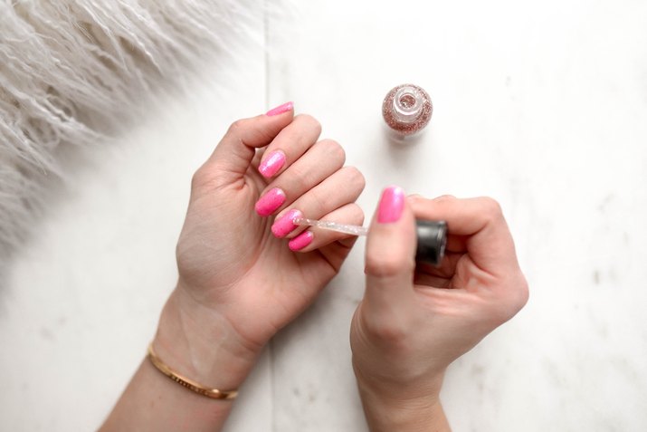 Cropped Hands Of Woman Applying Pink Nail Polish On Table