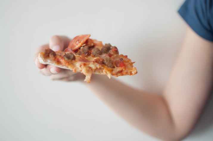 A young woman is eating a slice of pizza on a white background