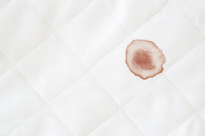 Blood stain on white mattress after night menstruation. Fresh or old stains cleaning from sheet of bed. Empty place for text. Close up. Top view.