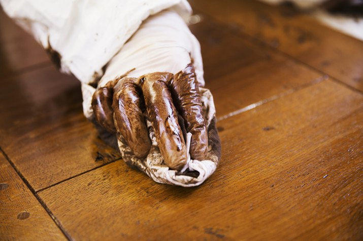 Close up of a carpenter wearing protective gloves, applying varnish onto a wooden surface with a cloth.