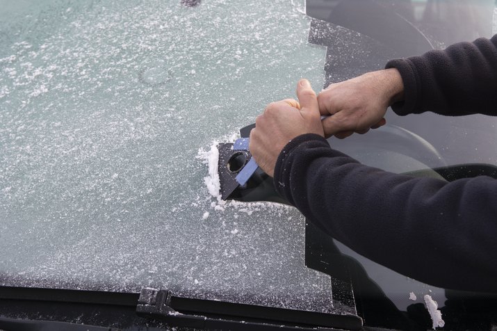 Close up of man using scraper to remove ice from windscreen