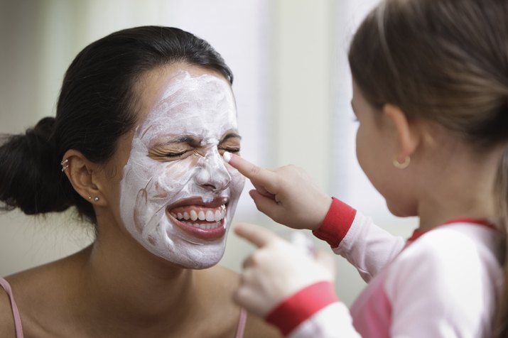 Daughter applying moisturizer to face of laughing mother
