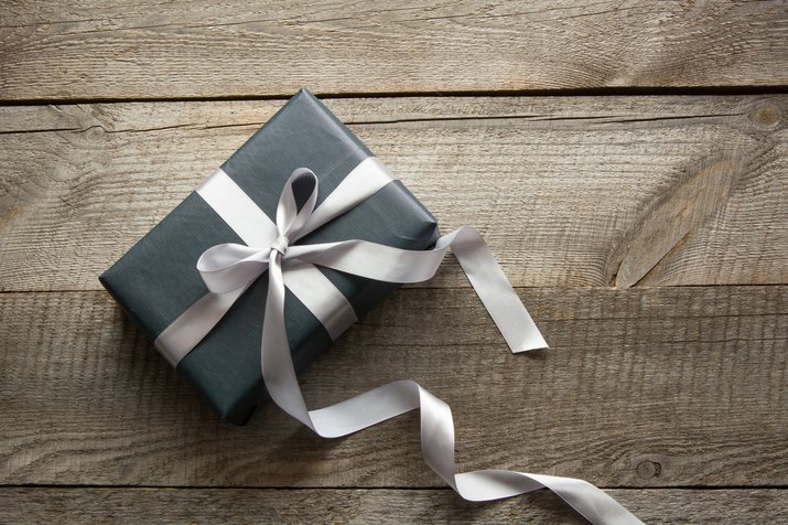 Gift box wrapped in black paper with ribbon on board.