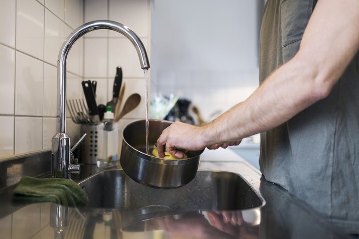 Midsection of man washing sauce pan with scouring pad at sink