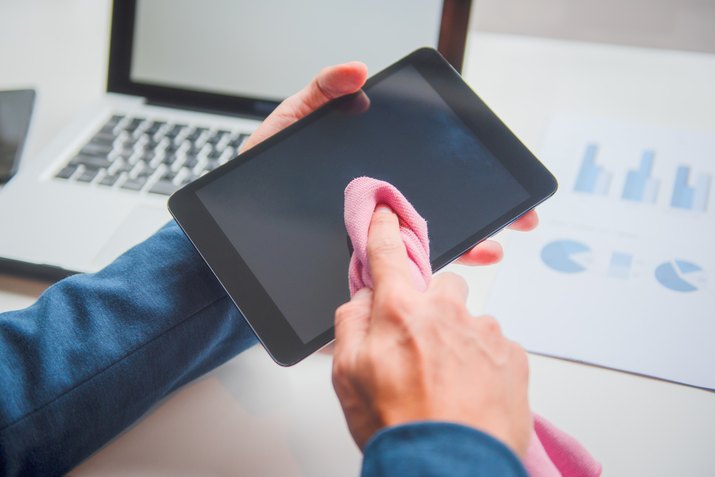 Cropped Hand Of Businessman Cleaning Digital Tablet Screen At Desk In Office