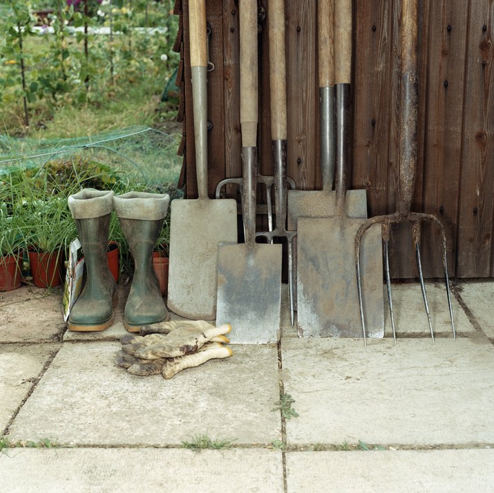 Spades, rake, boots and gardening gloves by a shed