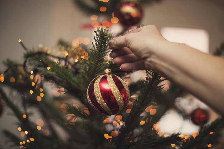 Woman holding Christmas bauble in front of illuminated Christmas tree
