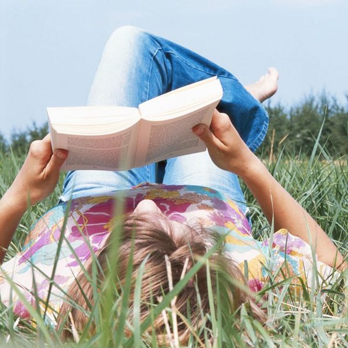 Young woman lying on field, reading book, ground view