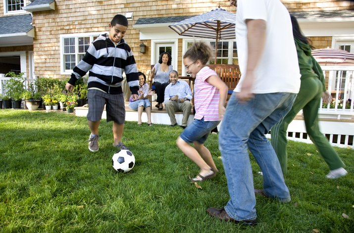 Family playing soccer in suburban backyard
