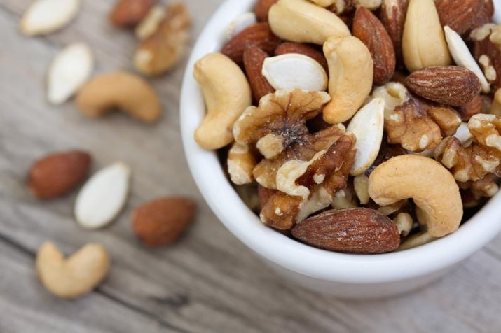 Bowl of mixed nuts on rustic wooden table in natural light.