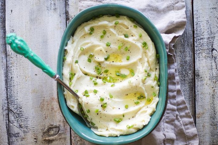 A blue dish full of whipped mashed potatoes topped with pats of butter and green onions