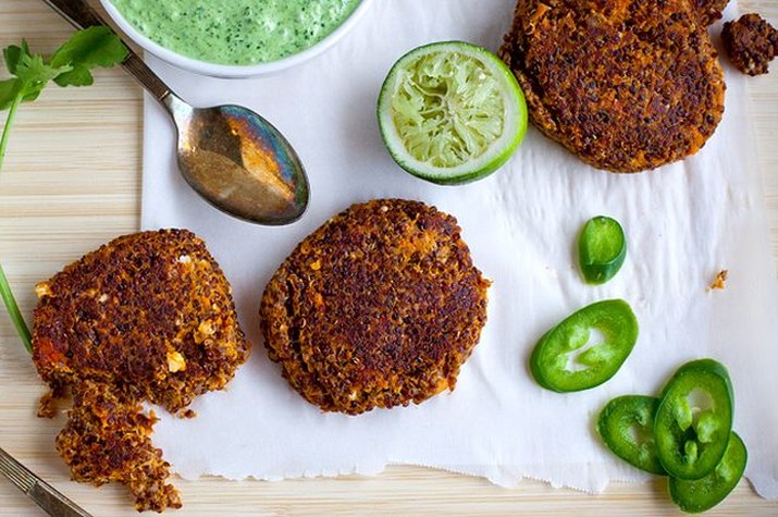 Sweet potato chipotle quinoa cakes on a cutting board with limes, sliced jalapenos and cilantro lime crema.