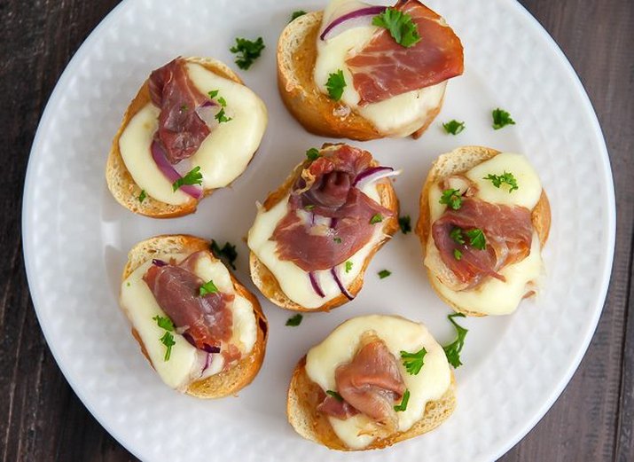 A plate of neatly compiled fig and prosciutto crostinis.