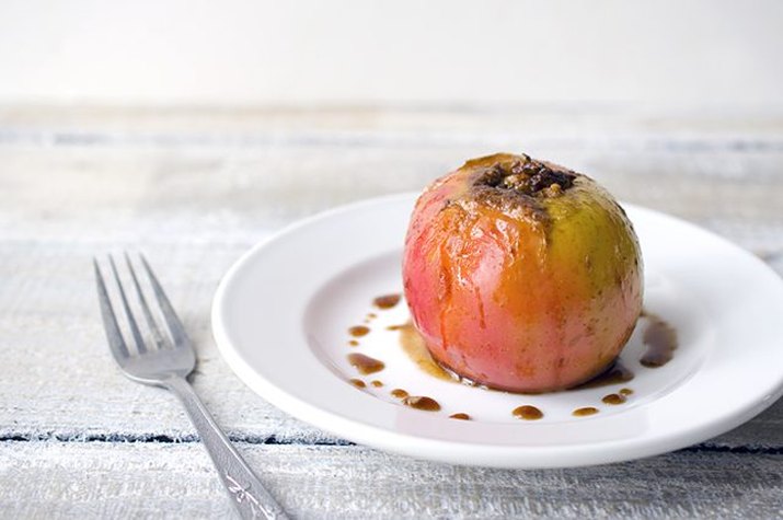 A freshly baked pecan-stuffed apple on a plate.