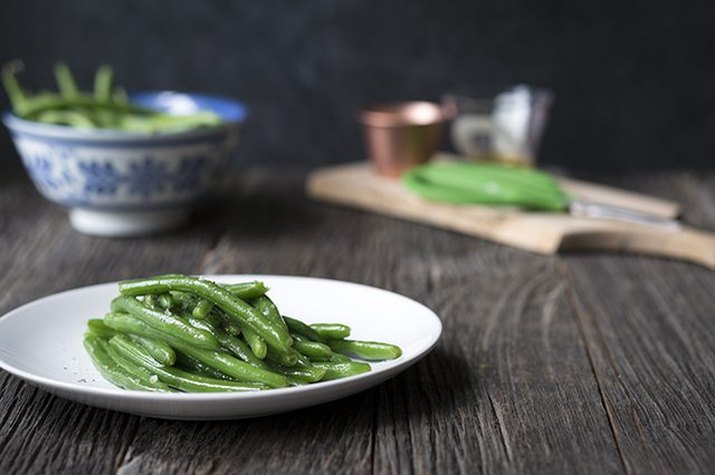 A plate of green beans in the foreground and a bowl of uncooked green beans in the background